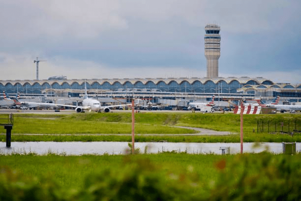 Airport view with aircraft and control tower, grassy foreground, overcast sky.